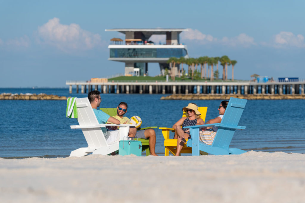 friends sitting in chairs on beach with pier in background